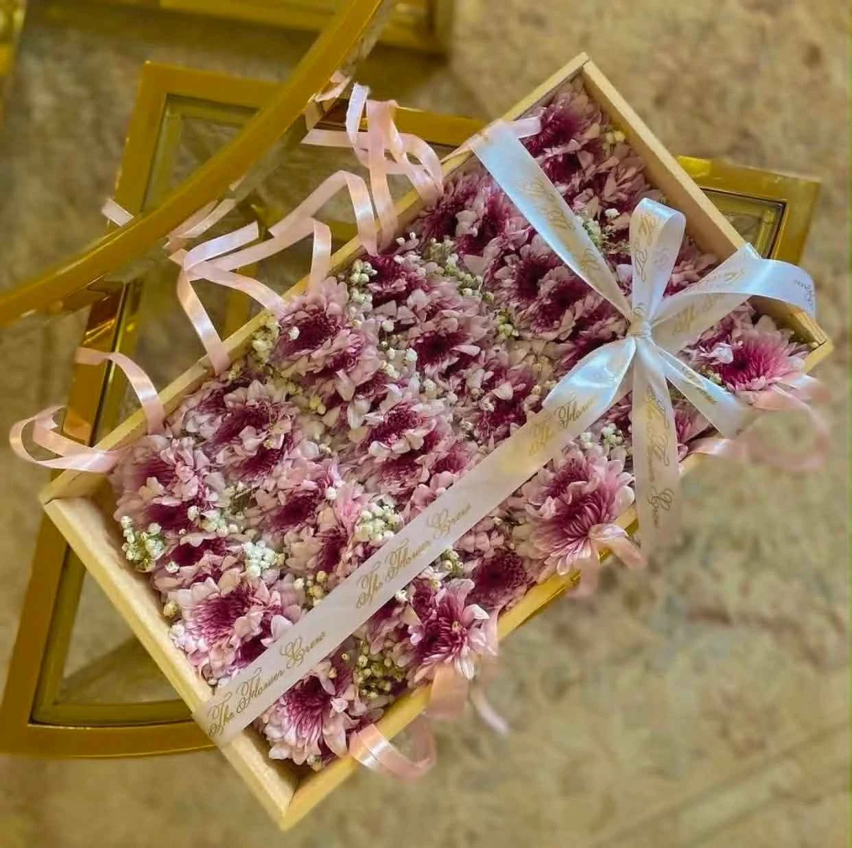 Luxury pink chrysanthemum gajra set with Baby’s Breath flowers presented in a wooden tray, customizable bridal floral accessories for weddings in Pakistan.