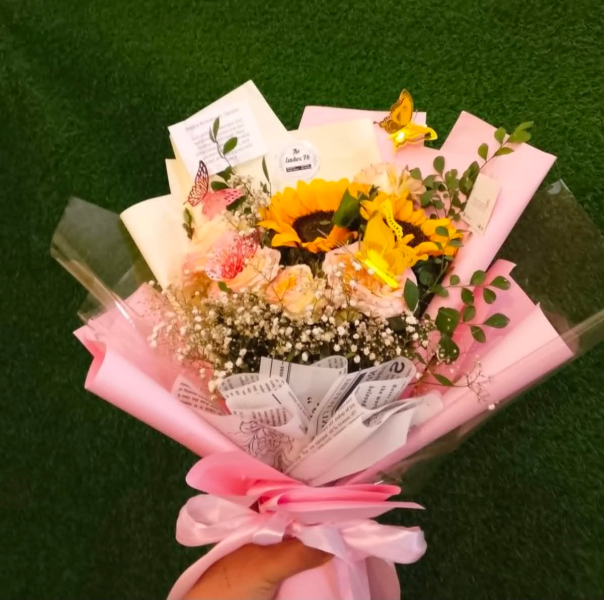 Cute mini sunflower bouquet with pink roses, butterfly decorations and elegant pink wrapping, perfect for birthdays and gifts for her in Islamabad.