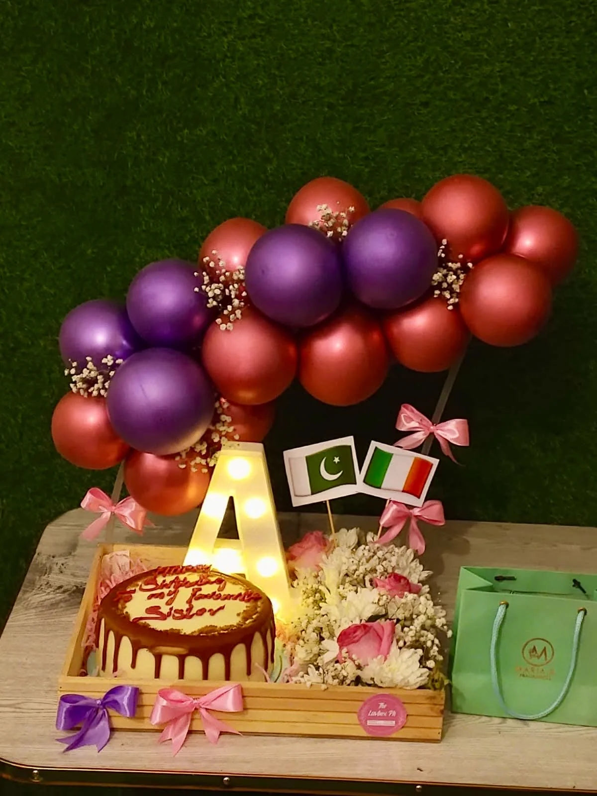 Sister gift in Pakistan with Layers Lotus cake Maria B perfume personalized LED initial flowers and balloon arch tray